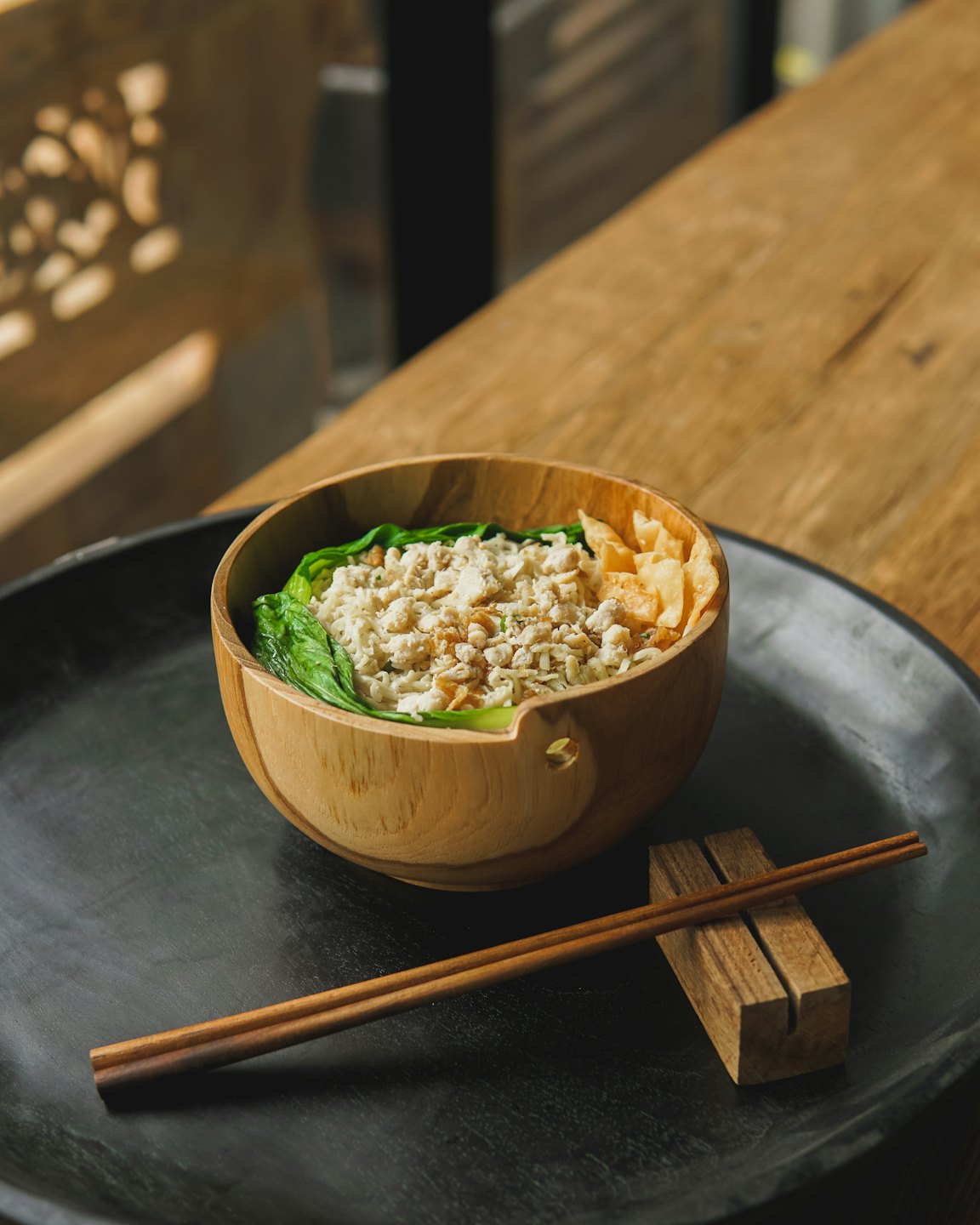 Noodle bowl with vegetables and protein on a wooden tray.