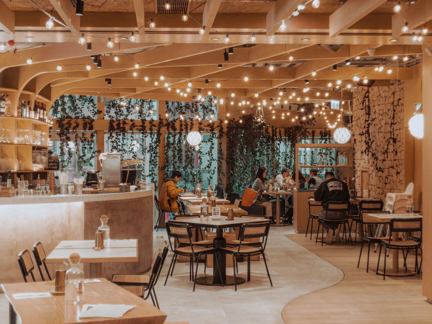 Customers dine and socialize inside a modern cafe with greenery.