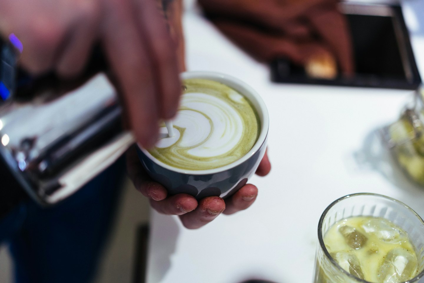 Barista pours steamed milk to create art in a matcha latte.
