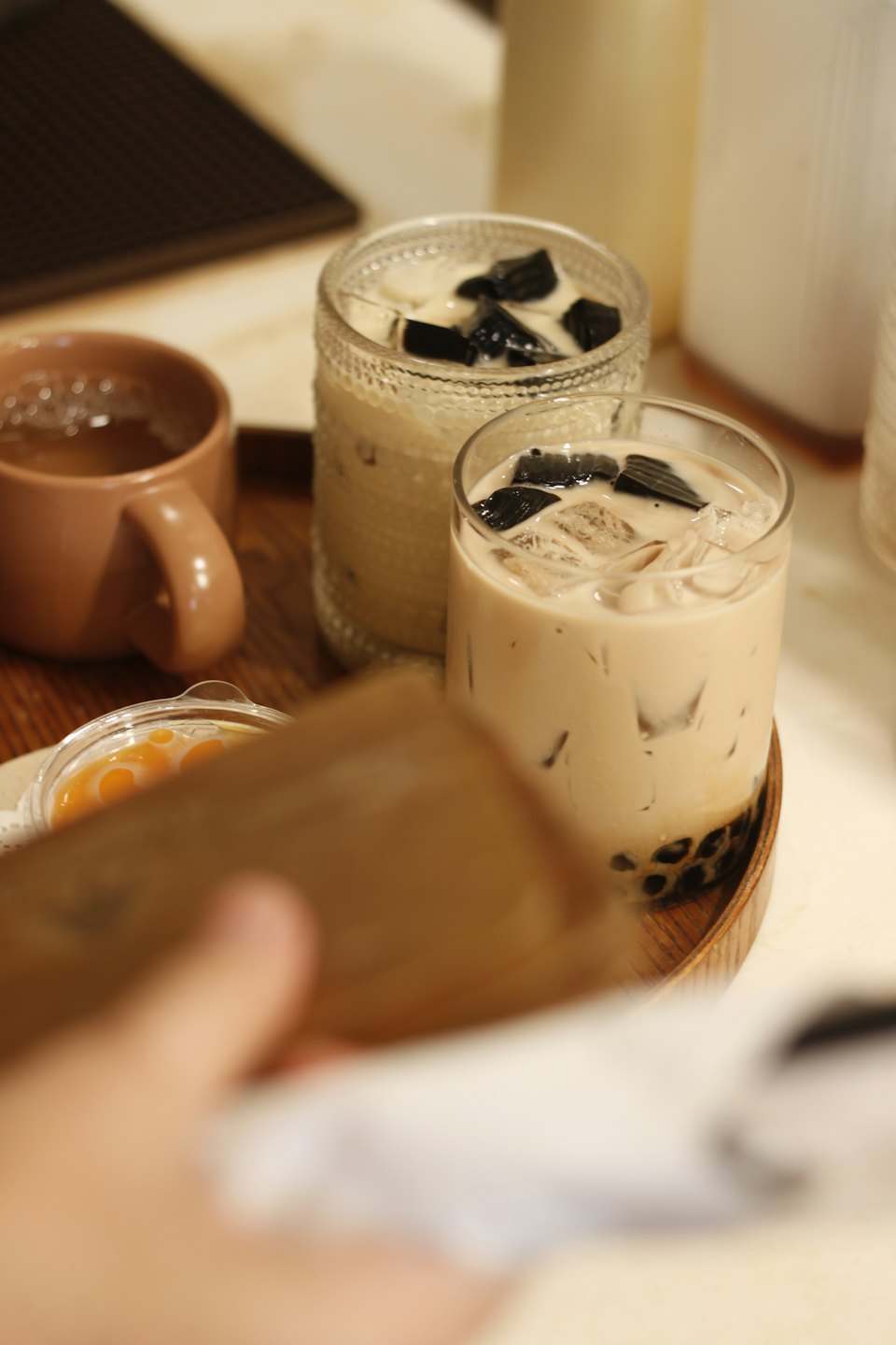 Two iced milky drinks and hot tea on a tray.