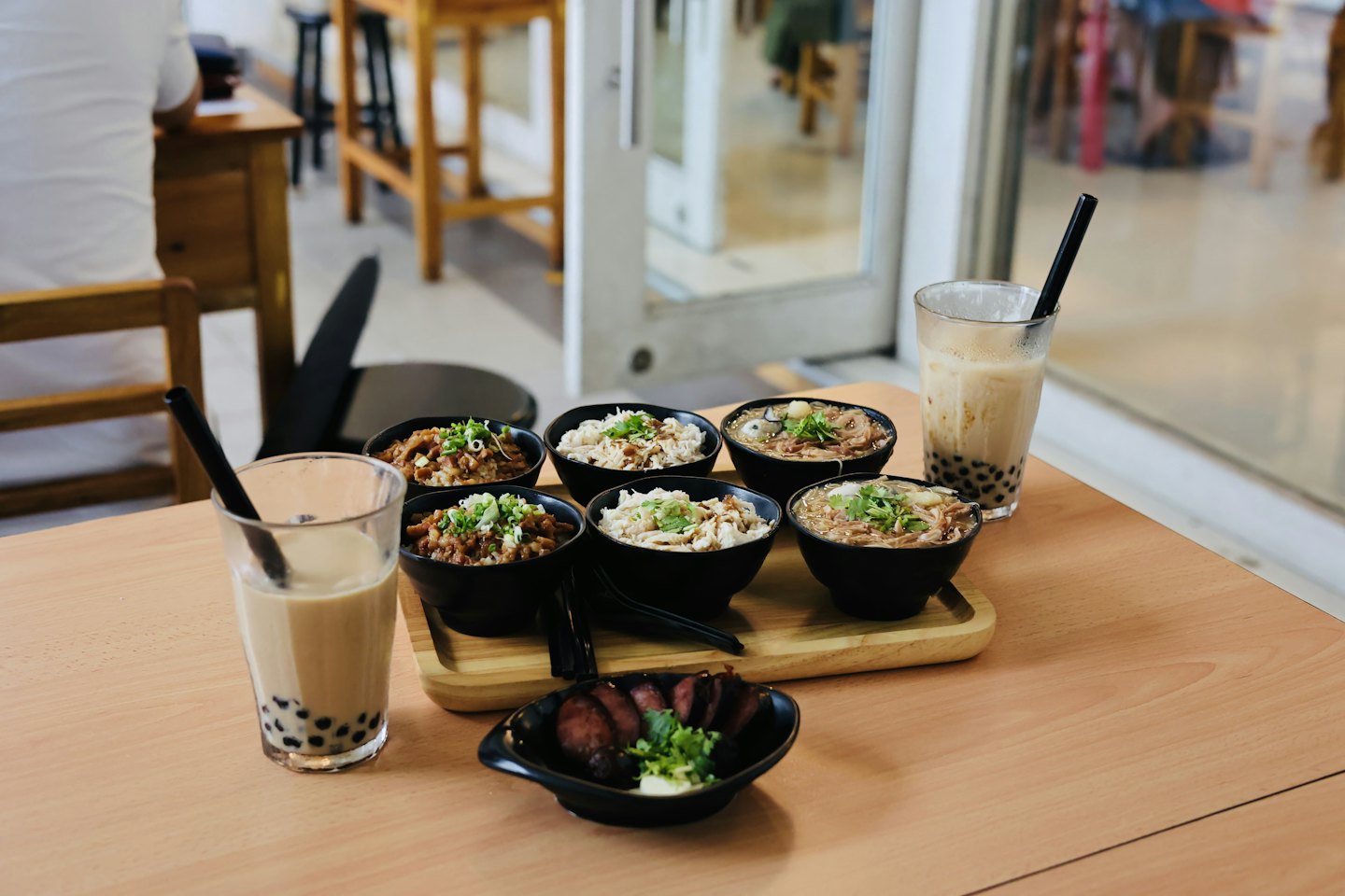 Assorted East Asian small dishes and bubble tea on a wooden table.