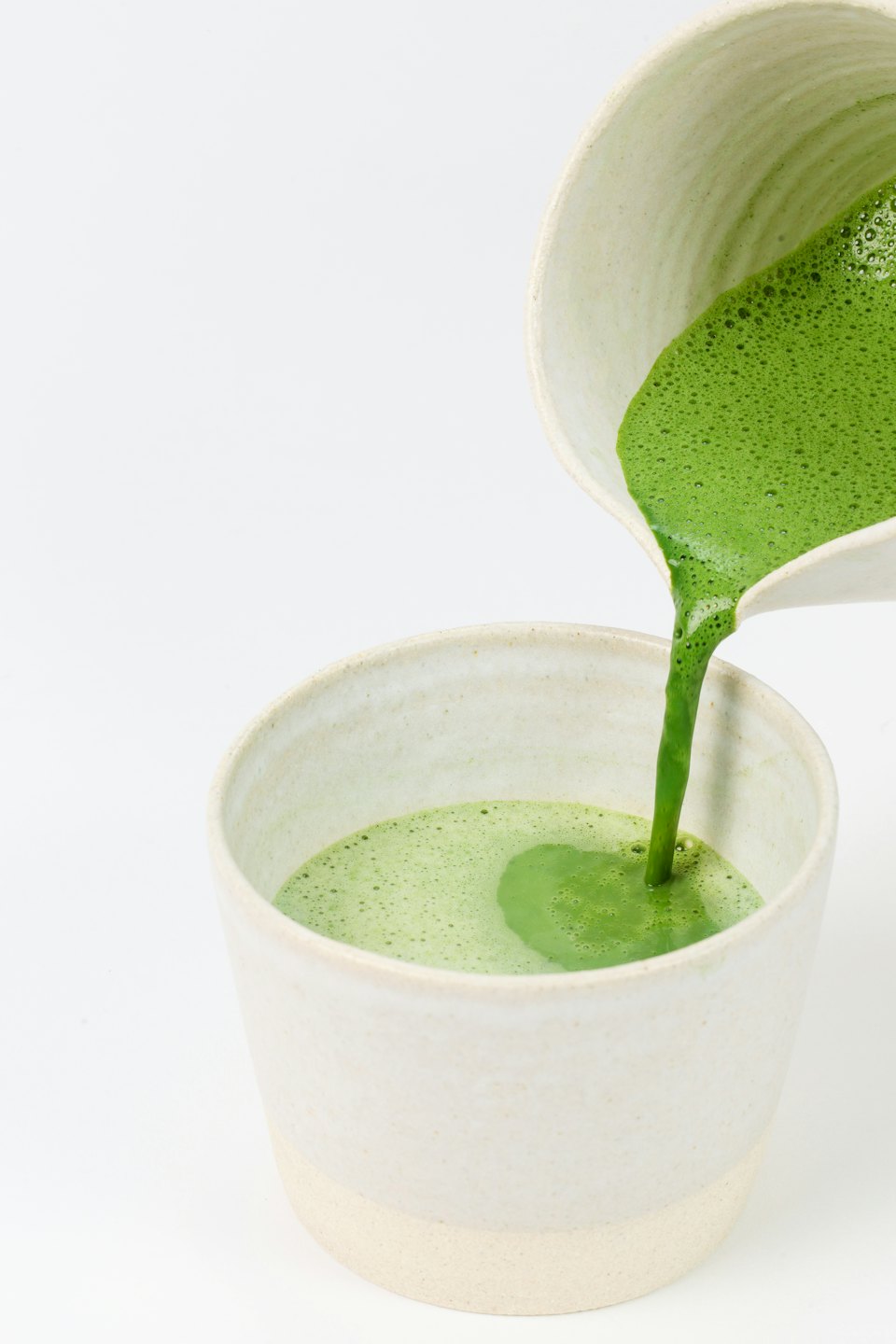 Green matcha latte pours from a ceramic pitcher into a cup.